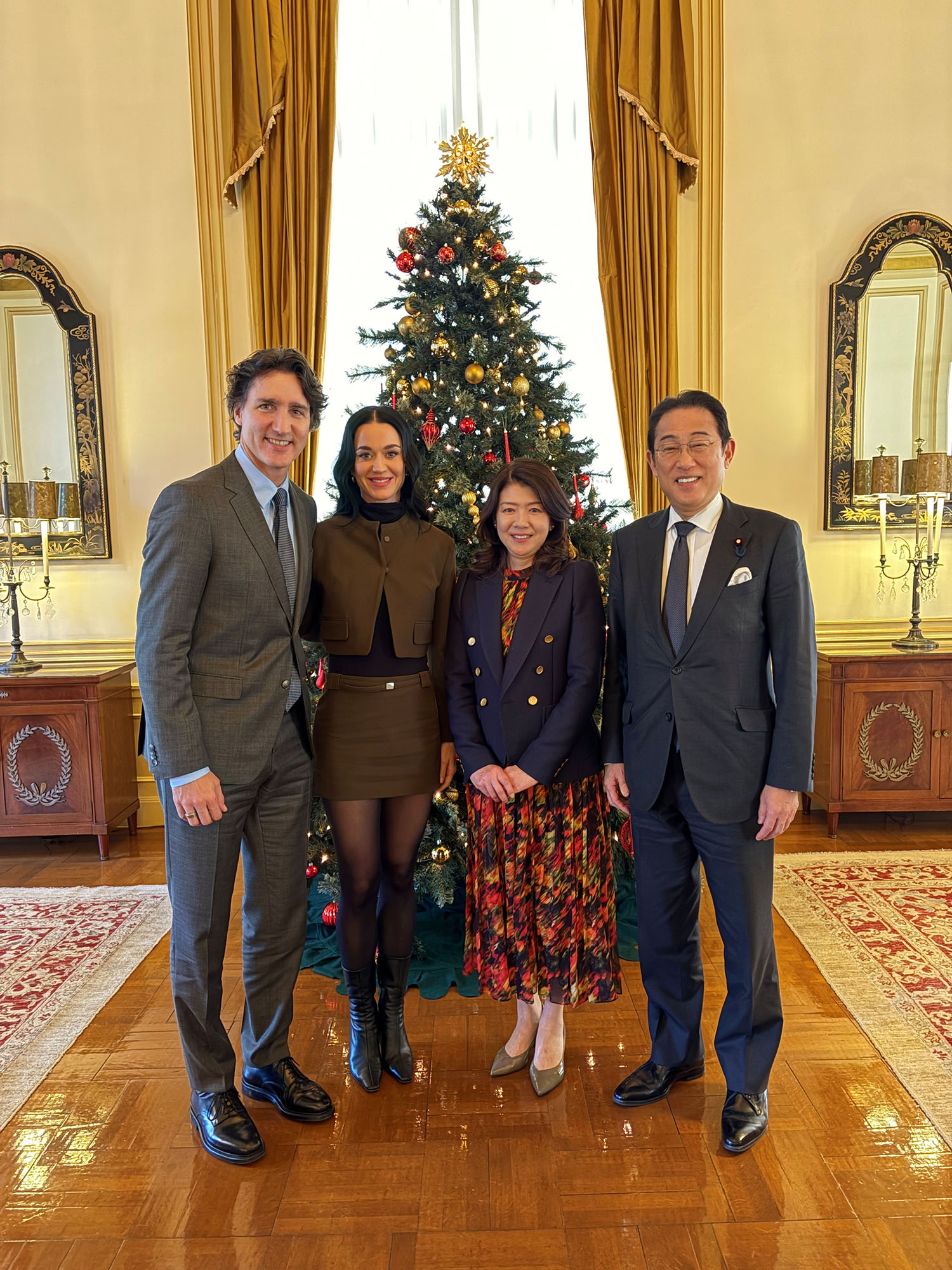 Katy Perry and Justin Trudeau with former Japan PM Fumio Kishida and his wife Yuko, standing in front of a Christmas tree.