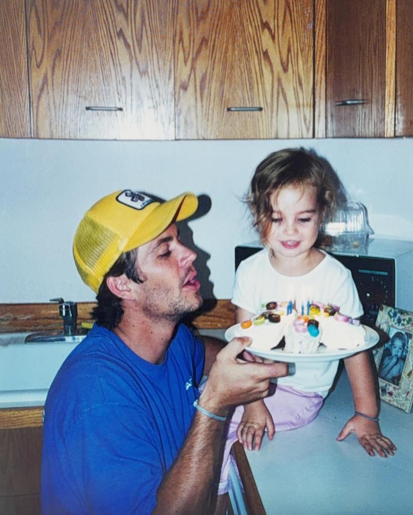 Paul Walker holds a butterfly-shaped birthday cake while daughter Meadow sits on a kitchen counter to blow out the candles.