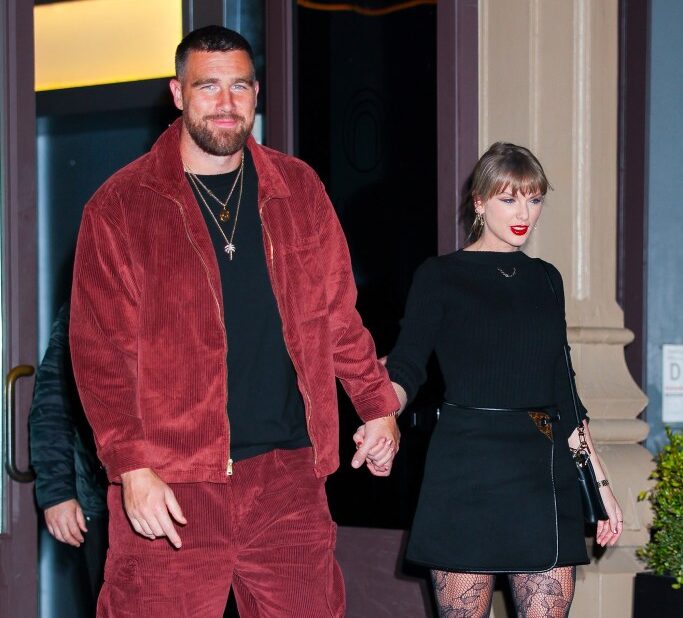 Taylor Swift and Travis Kelce holding hands while leaving a building.