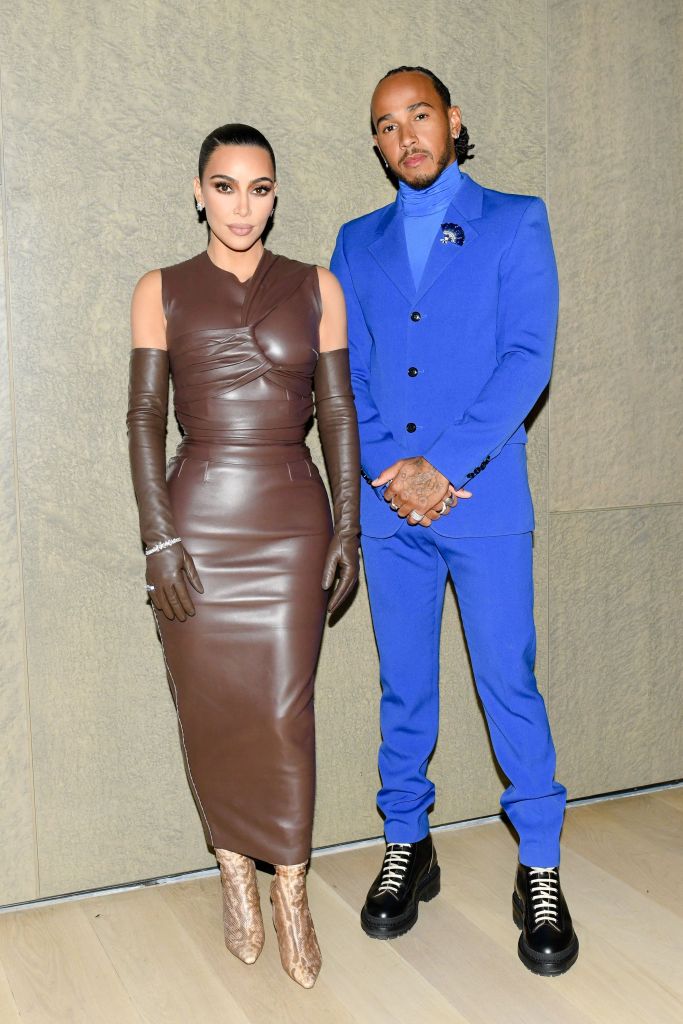 Kim Kardashian in a brown leather dress next to Lewis Hamilton in a blue suit.
