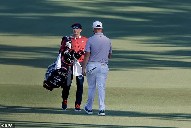 Sergio Garcia carries Jon Rahm's golf bag down the fairway as Rahm's caddie tends to a bunker shot.