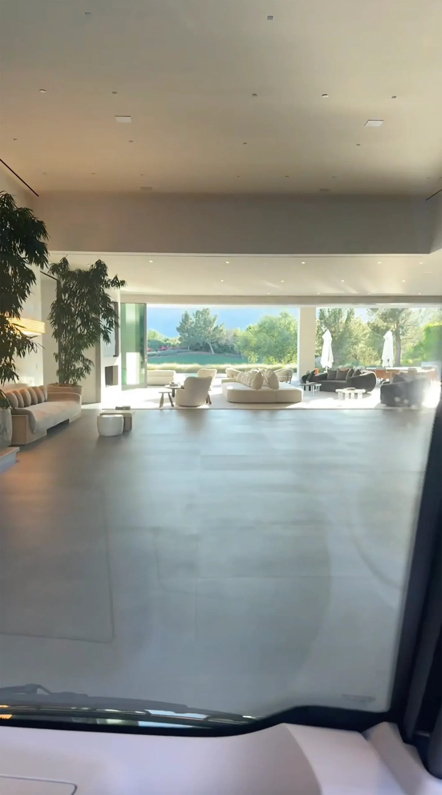 A spacious, modern living room with large glass doors that open to a lush green outdoor area.