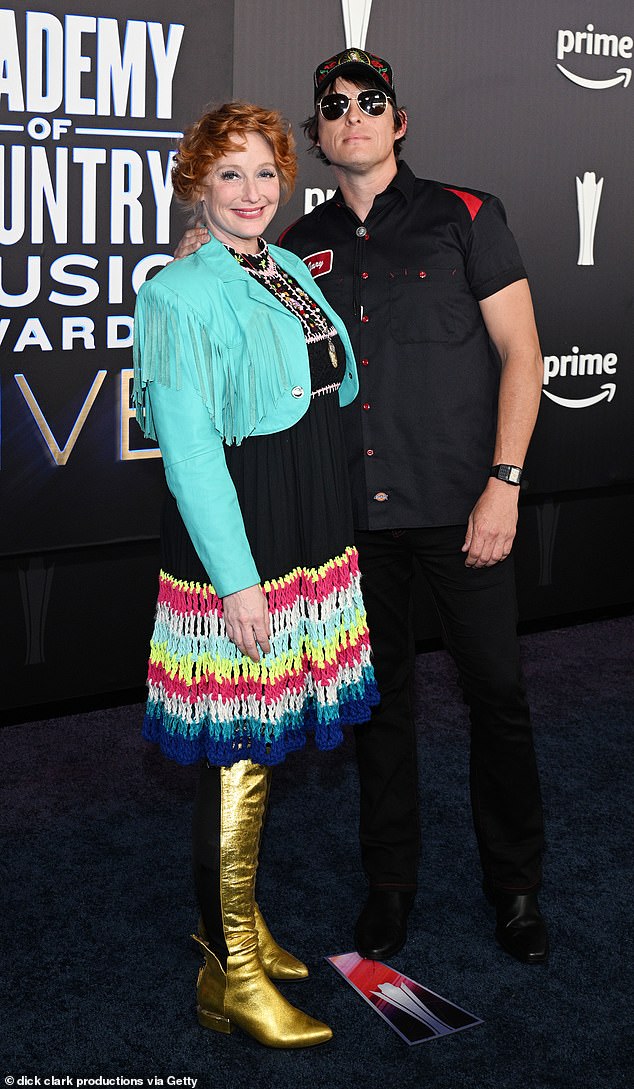 Leigh Nash in a black dress with rainbow-striped skirt, tasseled blue jacket, and metallic gold boots with Stephen Wilson Jr. at the ACMs