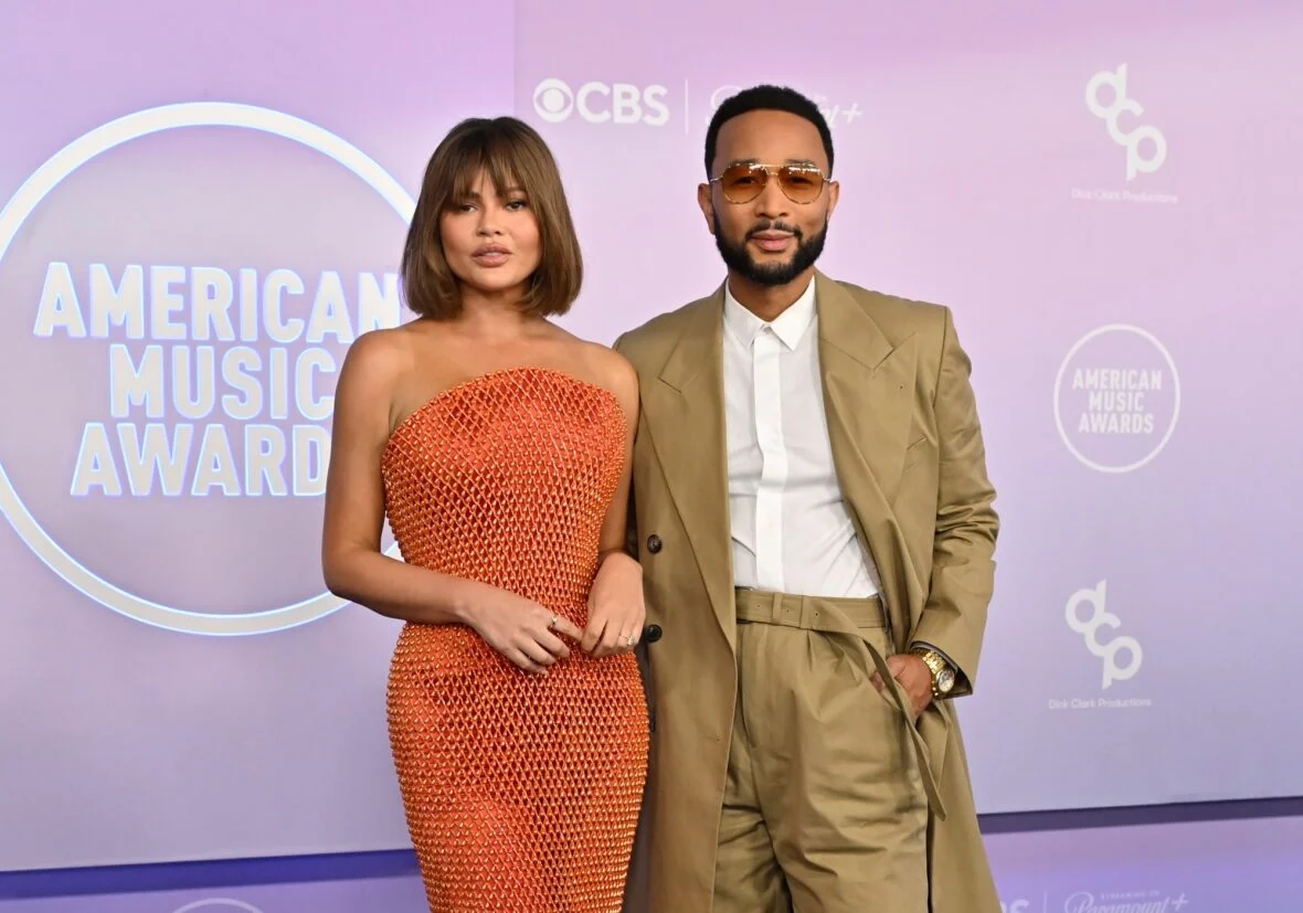 Teigen and Legend pose together on the AMAs carpet, highlighting her citrus-shimmer gown and his earth-tone tailoring.
