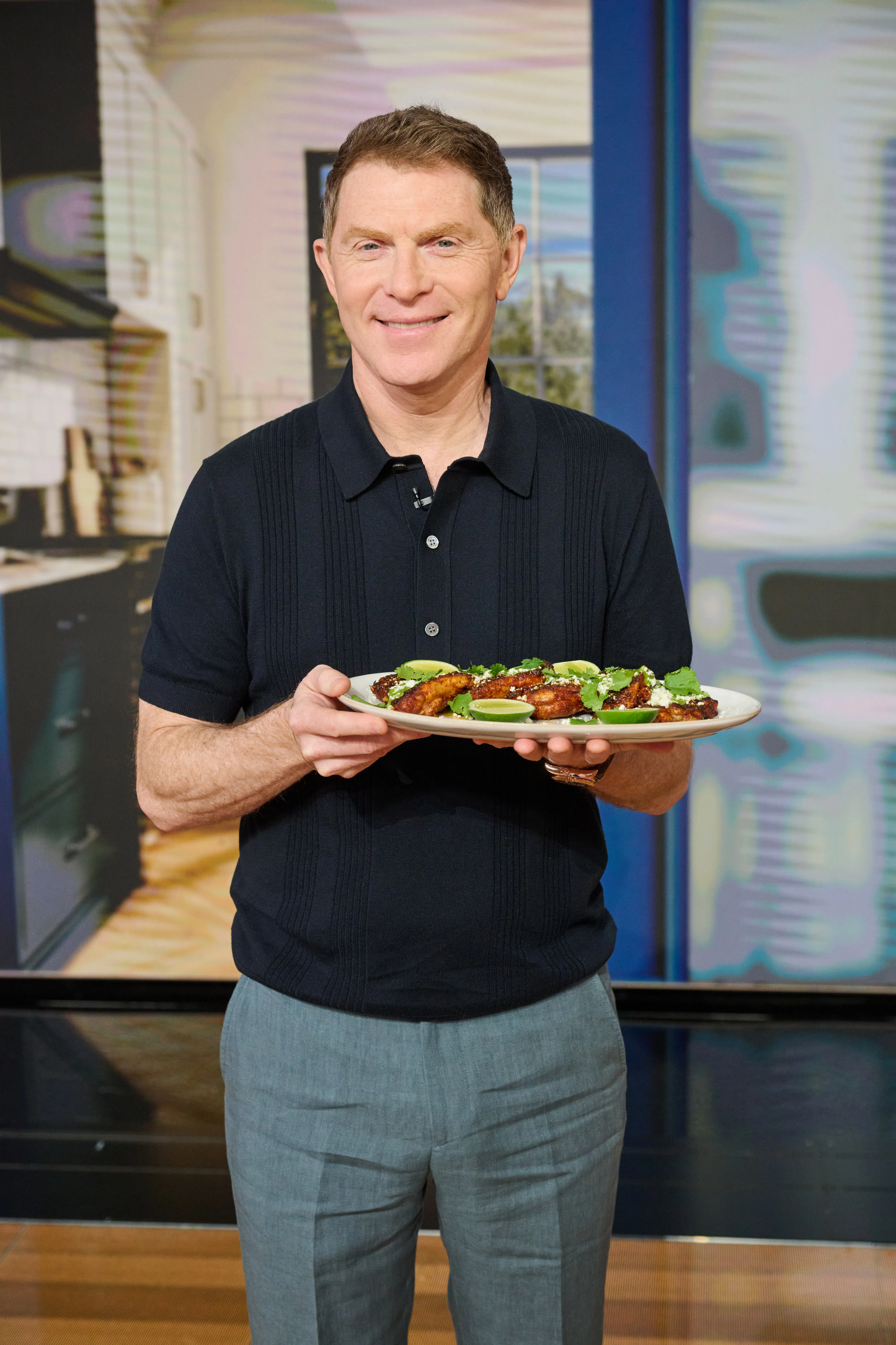 Bobby Flay holds a plate of chicken wings garnished with cilantro and lime.