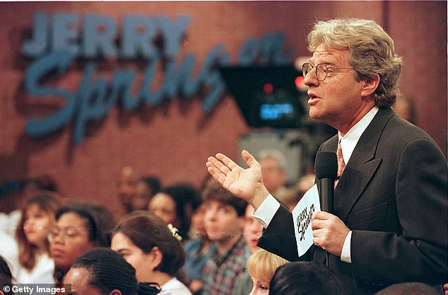 Jerry Springer hosting his daytime talk show, speaking to the audience with a microphone