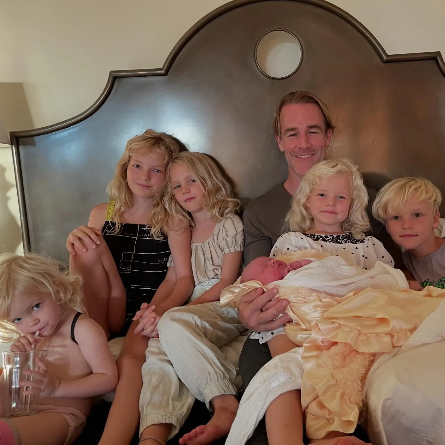 James Van Der Beek sits on a bed surrounded by his children, including a newborn.