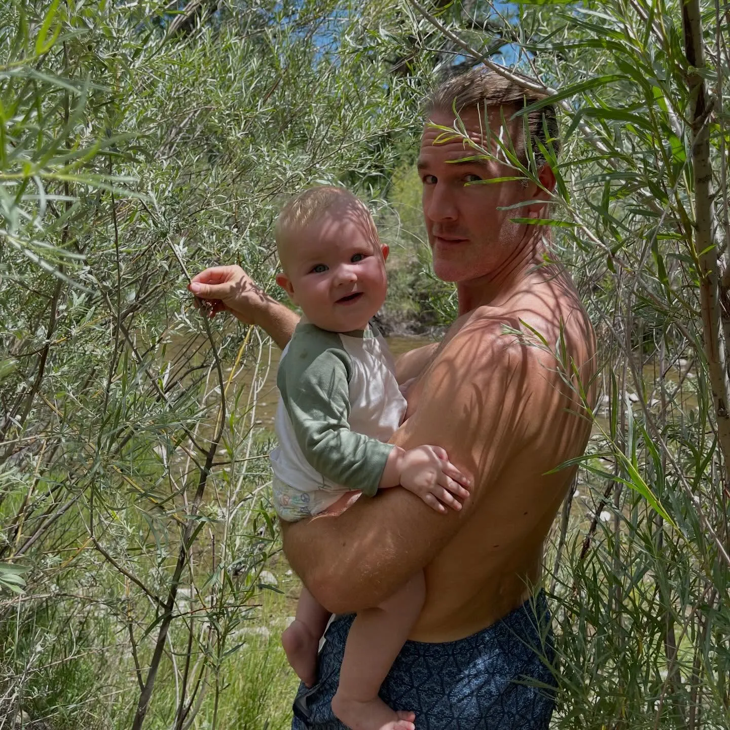 James Van Der Beek holds a baby beside a stream.