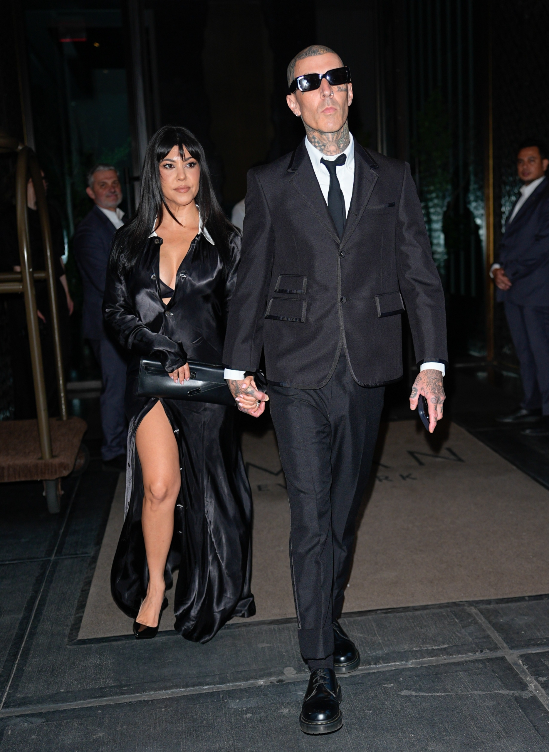Kourtney Kardashian and Travis Barker hold hands while leaving a New York hotel in coordinated black outfits.